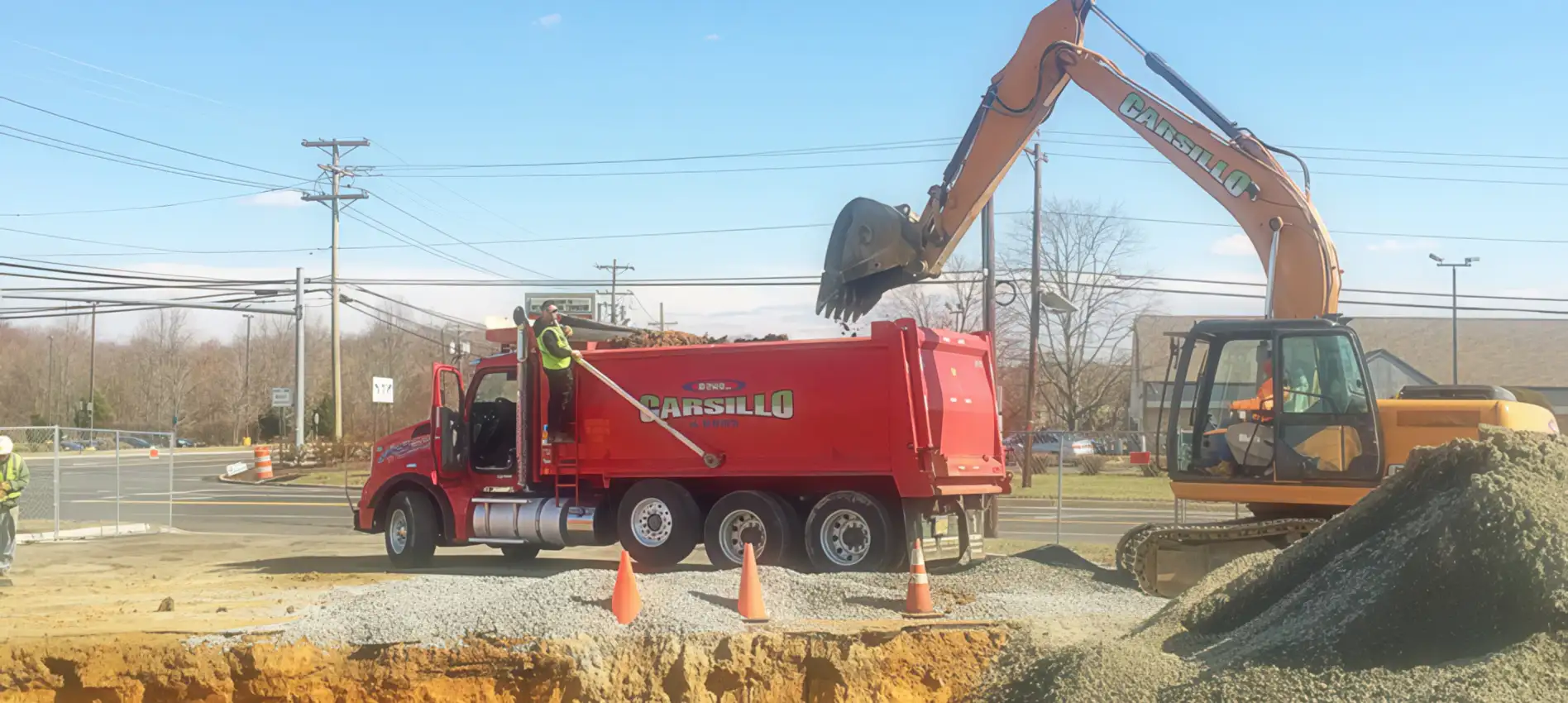 excavating2b Excavator loads dirt into the back of a red dump truck with the name Carsillo on the side.